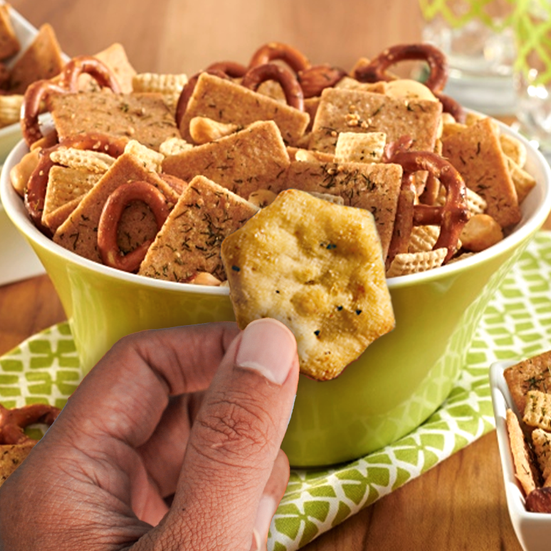 Bowl of cracker snack mix and hand holding up cracker.