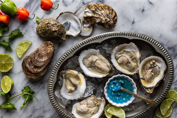 A top-down view of fresh oysters on the half shell, identical to the original arrangement but featuring a dish of bright blue sauce instead of red.