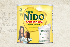 Nestlé NIDO Fortificada Dry Whole Milk can against a textured background with handwritten recipe text. / Lata de Nestlé NIDO Fortificada Dry Whole Milk sobre un fondo texturizado con texto de receta escrito a mano.