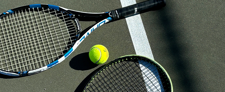 Two tennis rackets and a tennis ball laid on a green court.