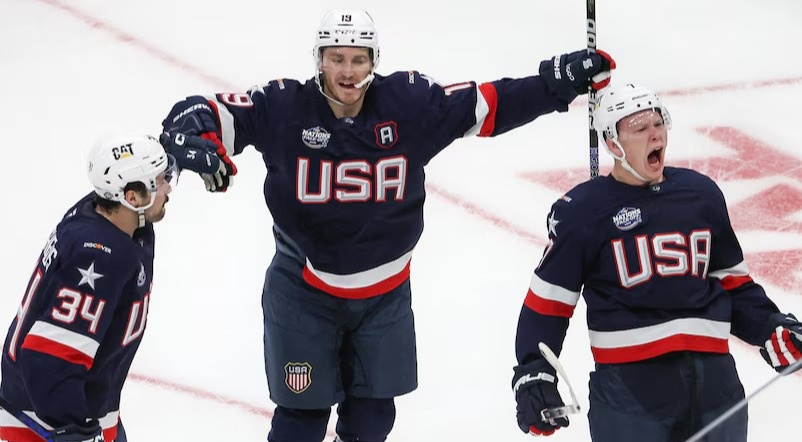 Three men wearing Team USA men's ice hockey uniforms cheer and celebrate while on the ice.