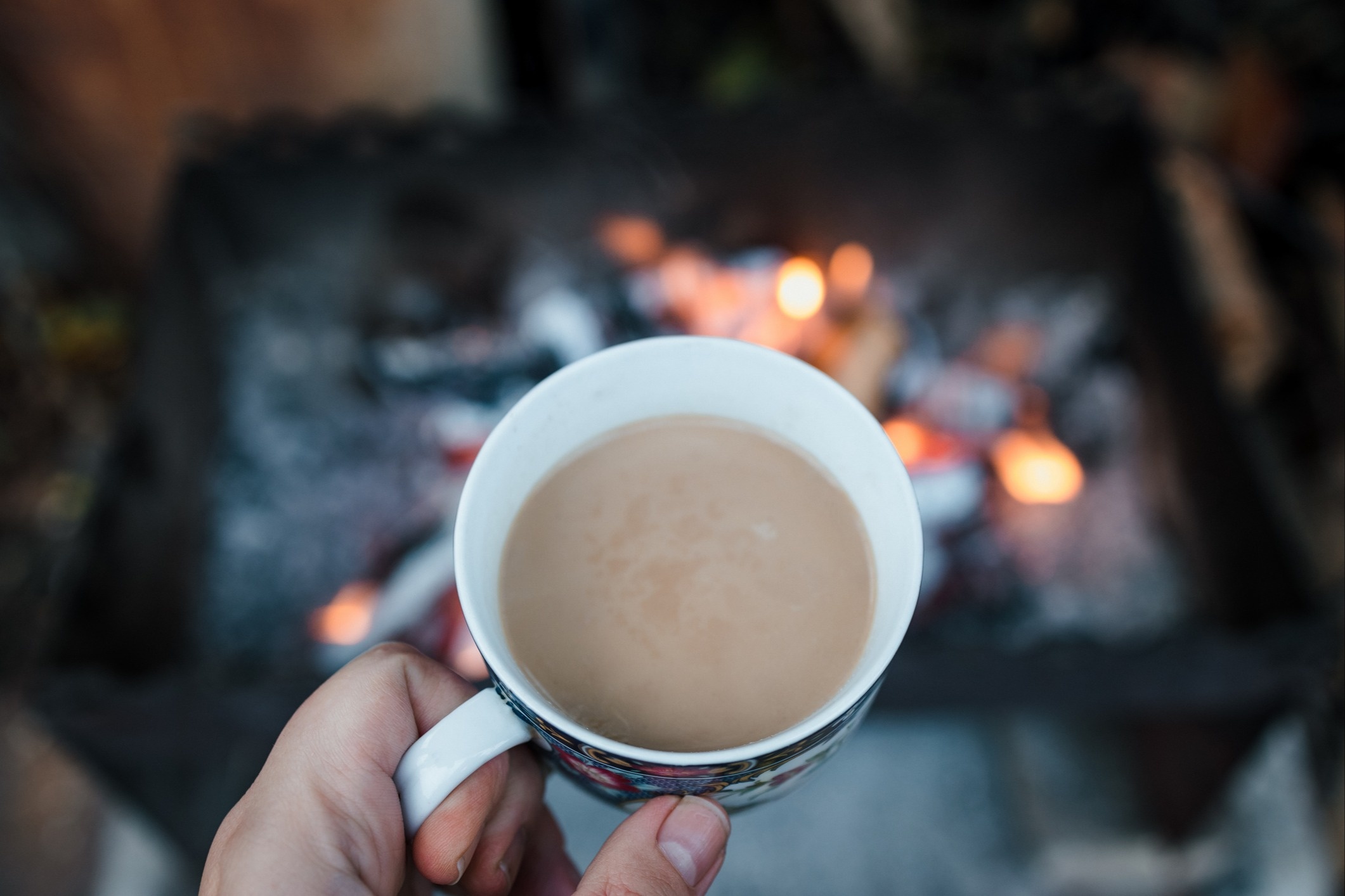 A mug of hot chocolate held in front of a blurry fire.