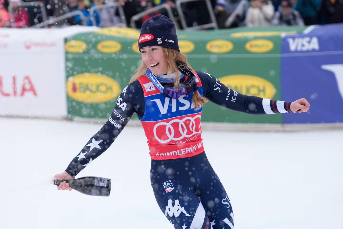 Mikaela Shiffrin, a blonde American skier, celebrates at the finish line with a bottle of champagne in hand after a recent competition win.