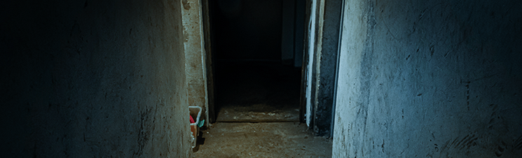 A dark, narrow concrete hallway leading into a shadowy doorway.