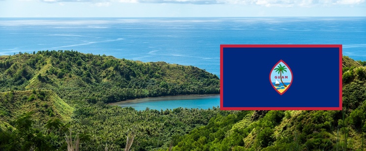 A scenic overlook of a lush green bay valley, with the flag of Guam overlaid on the right side.
