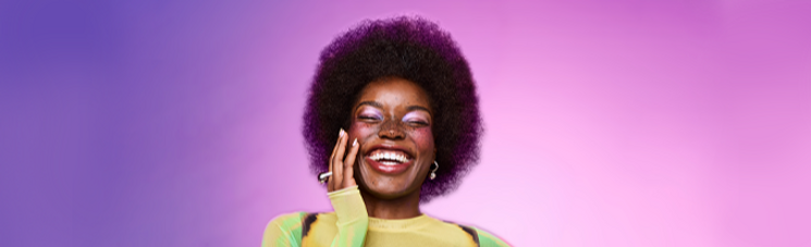 Smiling woman with curly afro against a purple and pink gradient background.