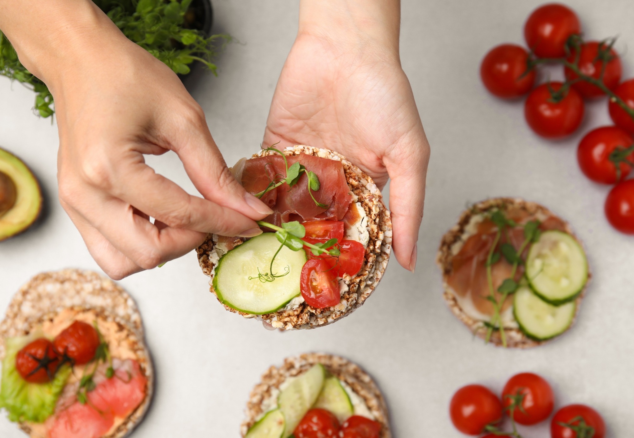 Person putting microgreens on a cracker with prosciutto and vegetables
