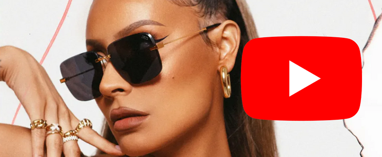 A close-up portrait of Desi Perkins wearing dark sunglasses with a YouTube play button logo layered on the right.