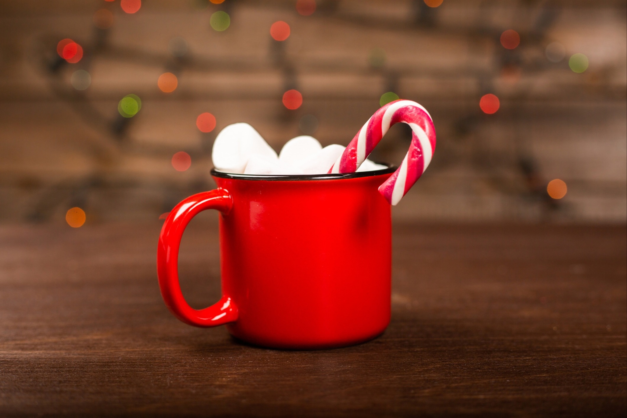 A red mug of hot chocolate sits on a wooden background with a large red and white candy cane sticking out the top of the mug.
