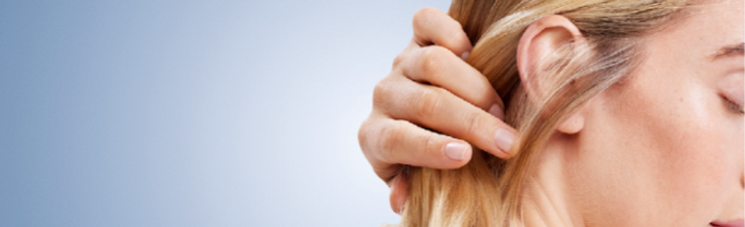Close-up profile of a woman running her fingers through her blonde hair against a light blue background.