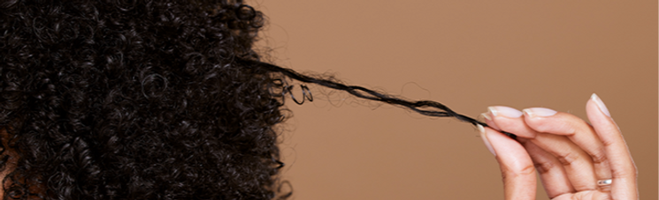 Close-up of curly hair strand being held to show curl pattern.