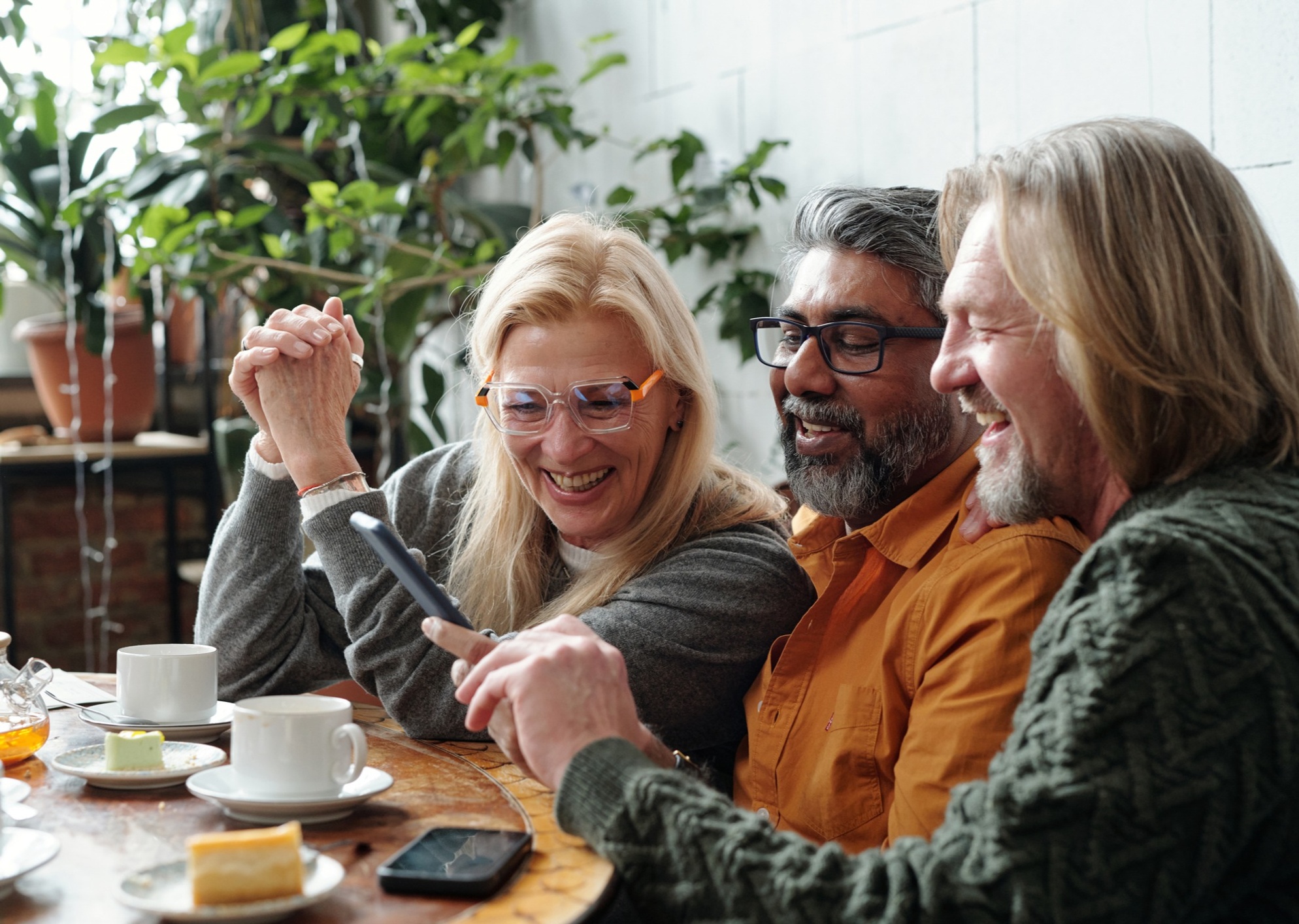 Middle-aged friends at a coffee shop laughing at something on the phone
