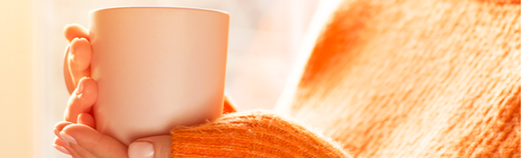 Person with orange sweater on and holding a mug