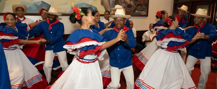 Dancers performing traditional Dominican merengue in colorful white, blue, and red traditional attire.