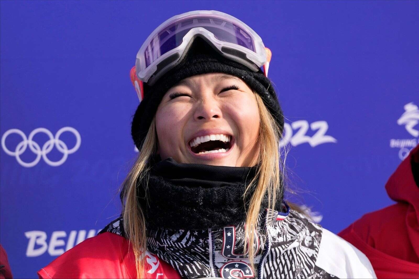 Chloe Kim, a young American athlete, grins in front of a blue wall after medaling at the 2022 Winter Olympic Games. 