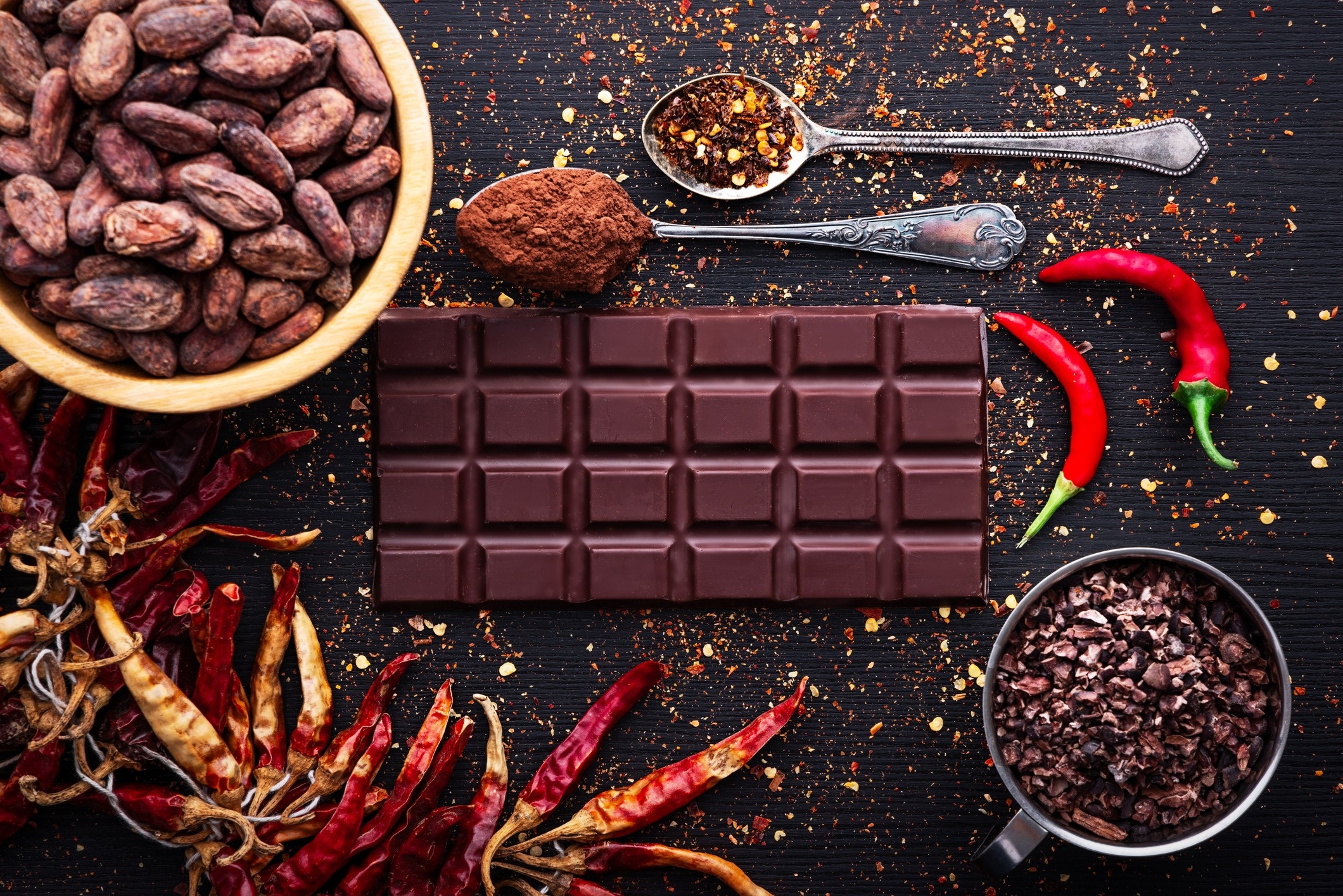 A bar of chocolate surrounded by peppers and pepper flakes.