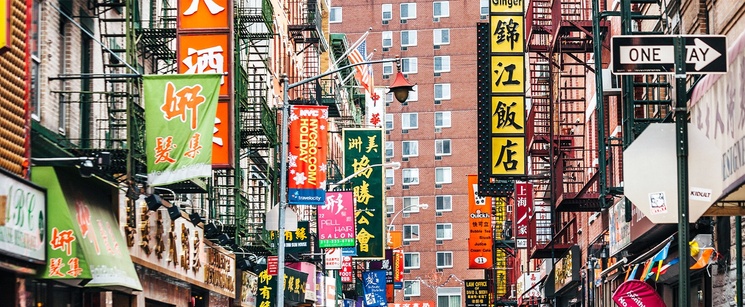 A bustling street scene in Chinatown featuring crowded buildings adorned with colorful, overlapping Chinese storefront signs.